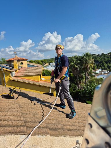 Hombre trabajando en el tejado con equipo de seguridad y cuerda de escalada.